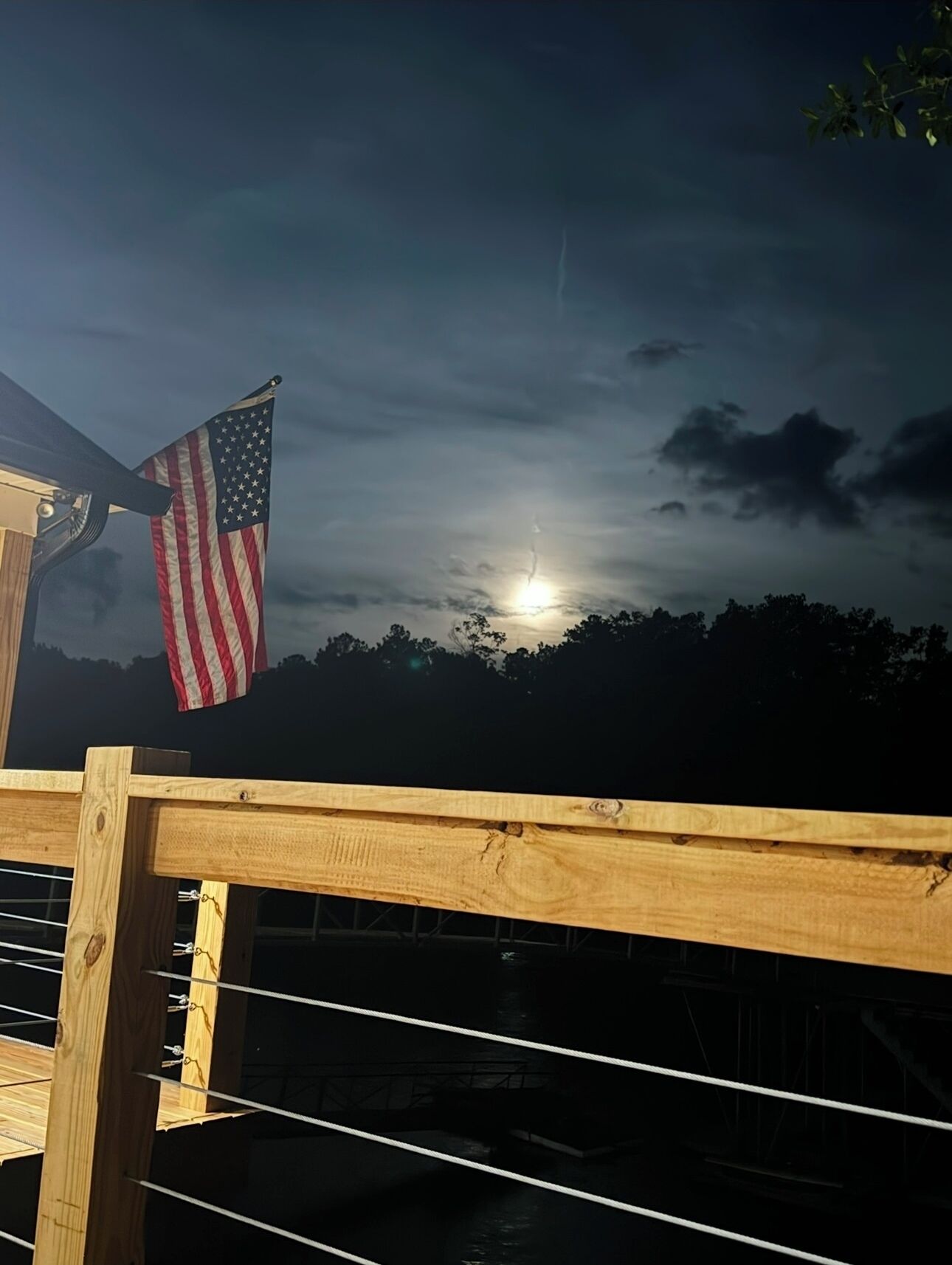 Eine Holzterrasse mit Metallgeländer, eine amerikanische Flagge und ein Blick auf den Mond über einer dunklen Landschaft.