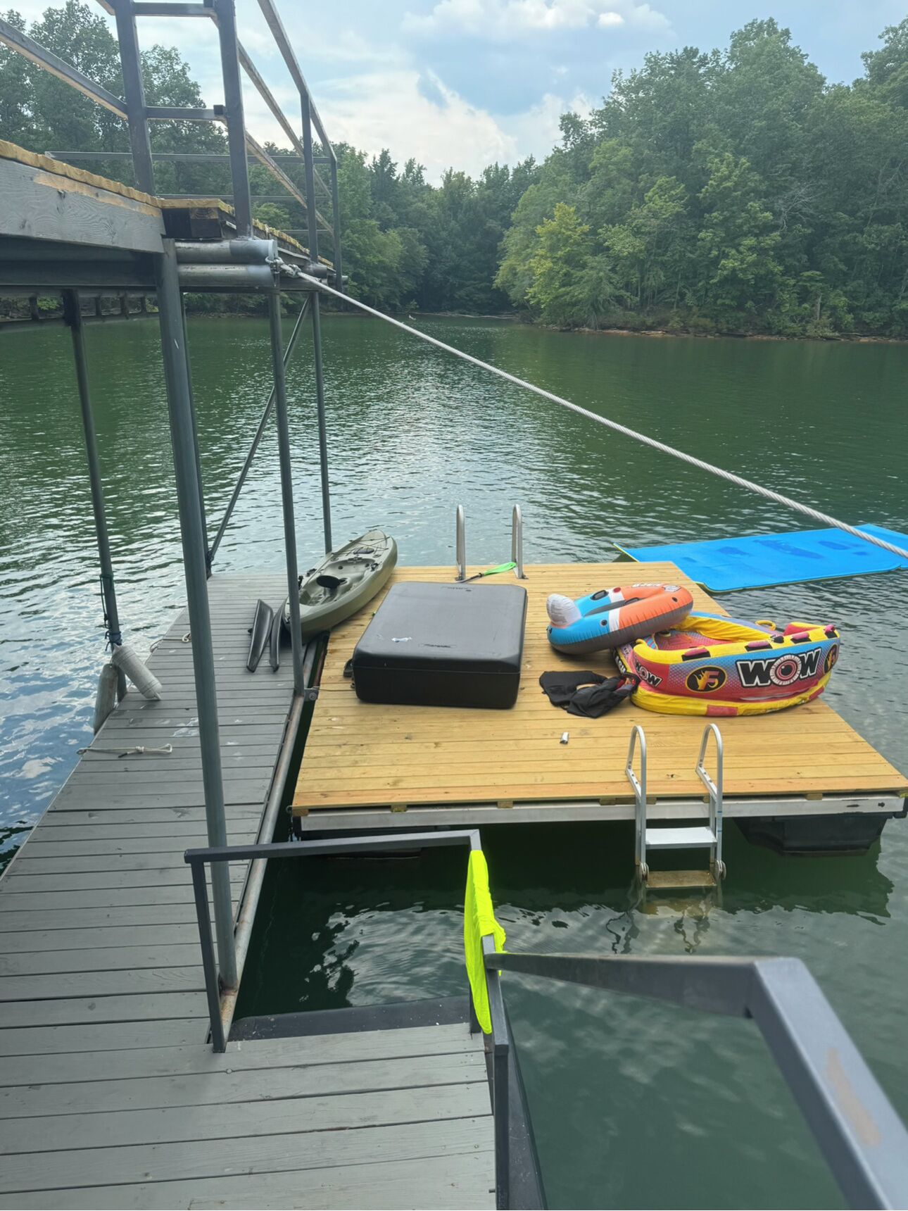 A wooden dock with a kayak, a life preserver, and a colorful inflatable ring on a calm river.