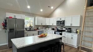 Una cocina moderna con armarios blancos, una isla central con taburetes, un refrigerador y un microondas.