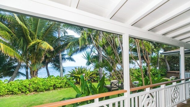 A covered outdoor area with a view of palm trees and the ocean.