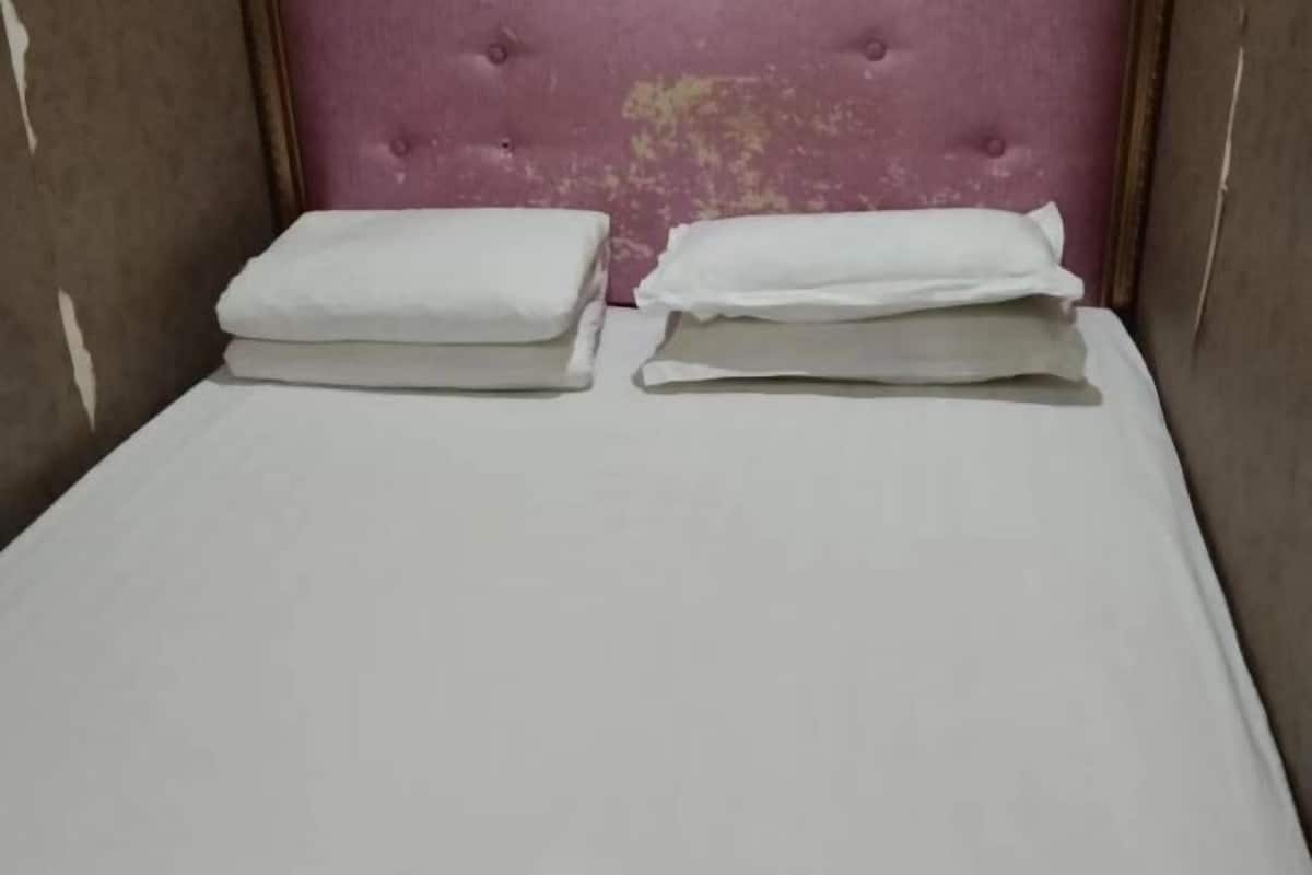 Un lit avec un matelas et des oreillers blancs, une tête de lit capitonnée et un mur sobre.