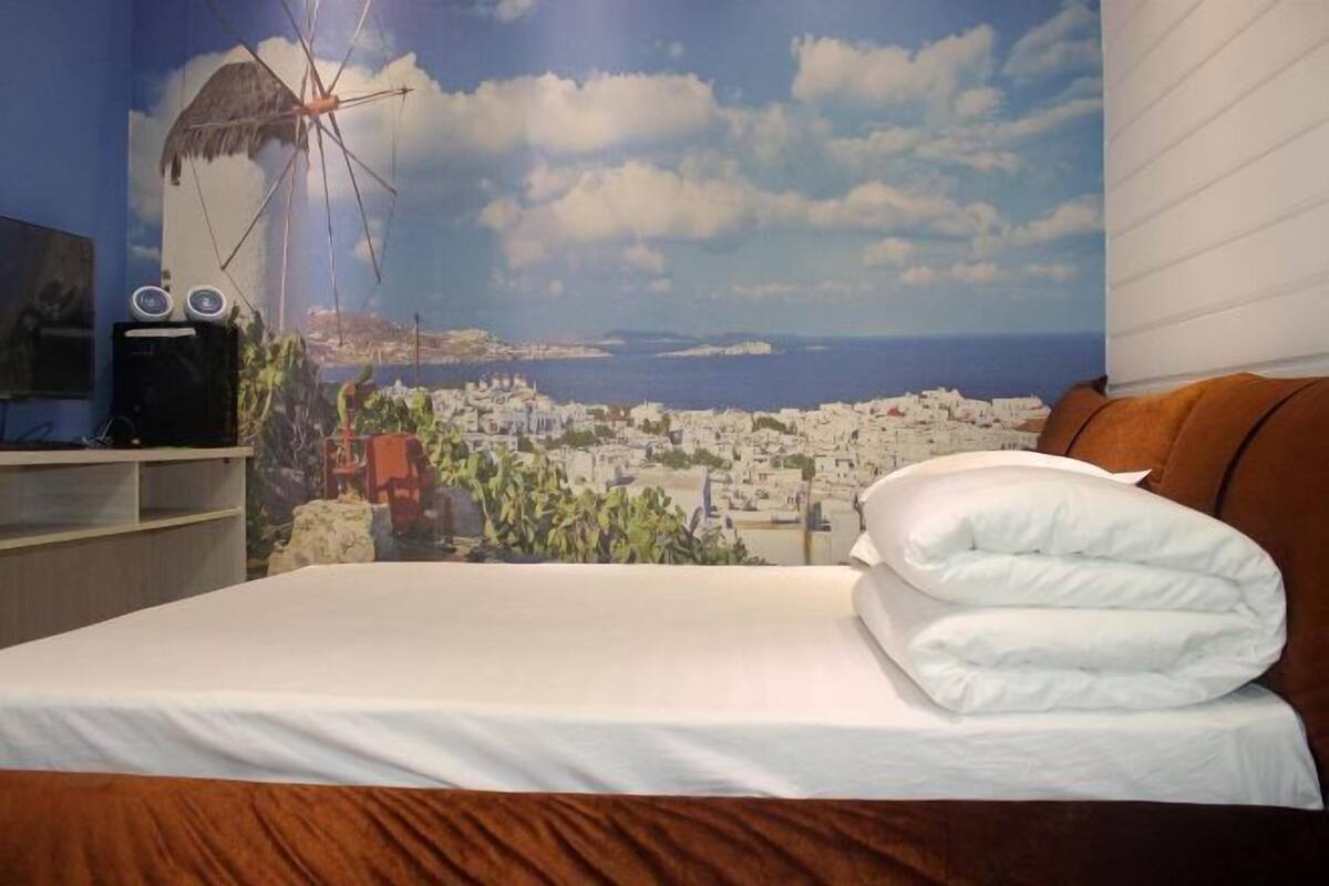 Une chambre d’hôtel avec un lit, une télévision et une fresque murale représentant un paysage urbain côtier.