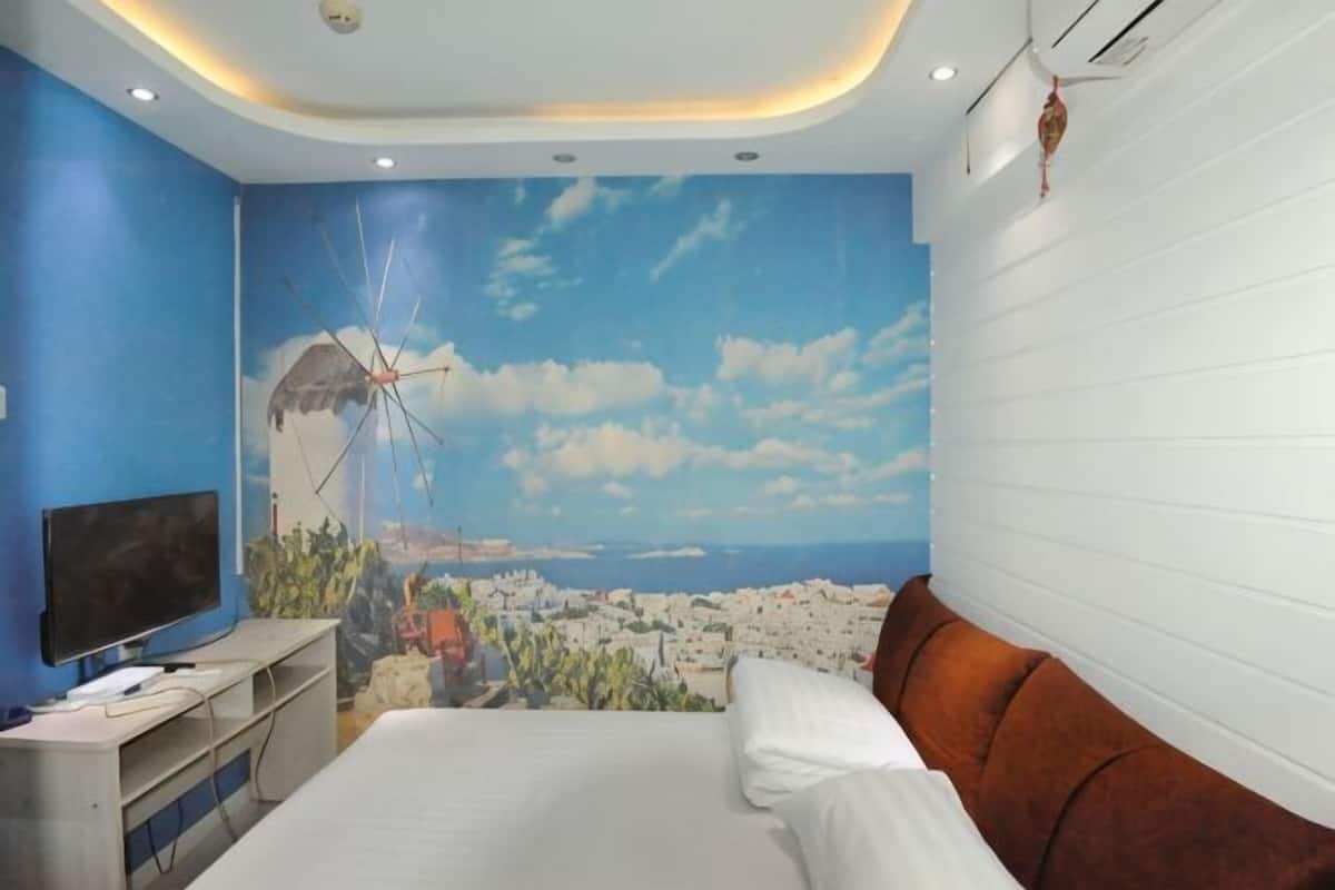 Une chambre à coucher avec un lit, un téléviseur et une fresque représentant un paysage urbain côtier.
