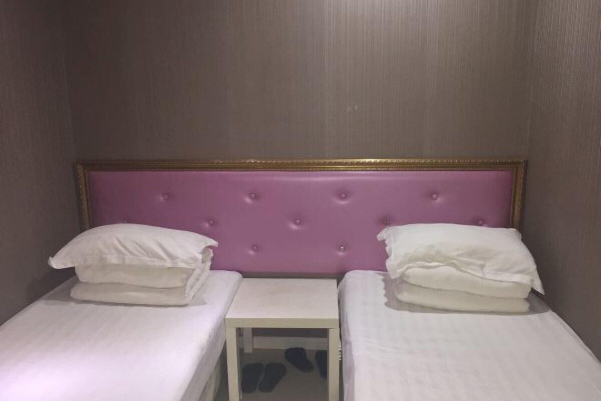 A small room with two single beds, each with a white mattress and pillows, and a purple tufted headboard.