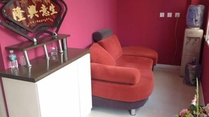 Ein Zimmer mit einem roten Sofa, einem kleinen weißen Schrank, einem Zier-Spiegel und einem Wasserspender.