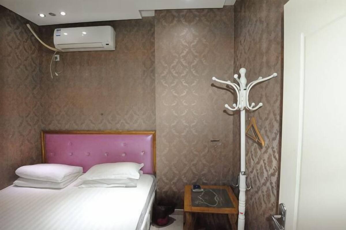 Une chambre d’hôtel équipée d’un lit, d’un appareil de climatisation, d’un porte-manteau et d’une petite table.