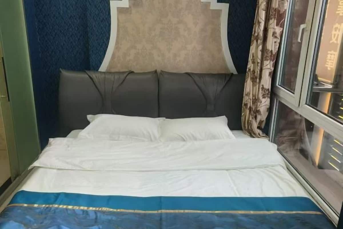 Un lit avec une literie blanche et bleue, une tête de lit sombre et une fenêtre avec des rideaux.