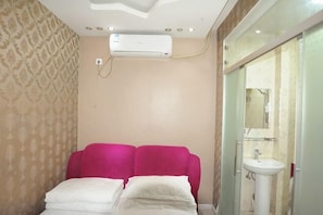 Een hotelkamer met een bed, een badkamer met een wastafel en spiegel, en een airconditioning.