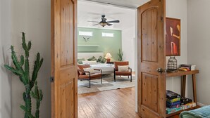 A room with a wooden door leading to a bedroom with a bed, two chairs, a ceiling fan, and a bookshelf with books. - Luxury Amenity Paradise! Sleeps 18 - Pool, Hot Tub, Game Room, Golf, Fire Pit!
 (Albuquerque)
