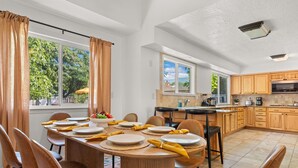A dining area with a round table set for four, wooden cabinets, and a kitchen with a large window. - Luxury Amenity Paradise! Sleeps 18 - Pool, Hot Tub, Game Room, Golf, Fire Pit!
 (Albuquerque)