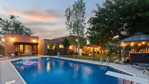 A swimming pool with lounge chairs and a gazebo, surrounded by trees and buildings. - Luxury Amenity Paradise! Sleeps 18 - Pool, Hot Tub, Game Room, Golf, Fire Pit!
 (Albuquerque)