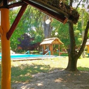 A tree with a nest in its branches, a wooden structure, and a swimming pool in the background. - Cabañas las 15 Marias  (San Rafael)