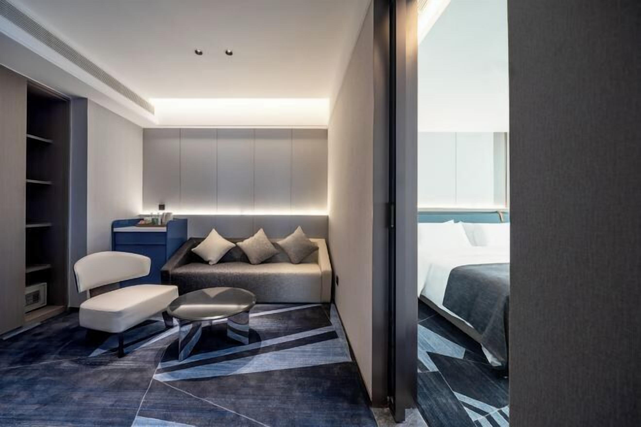 Ett modernt hotellrum med en soffa, ett litet bord, en garderob och en säng.