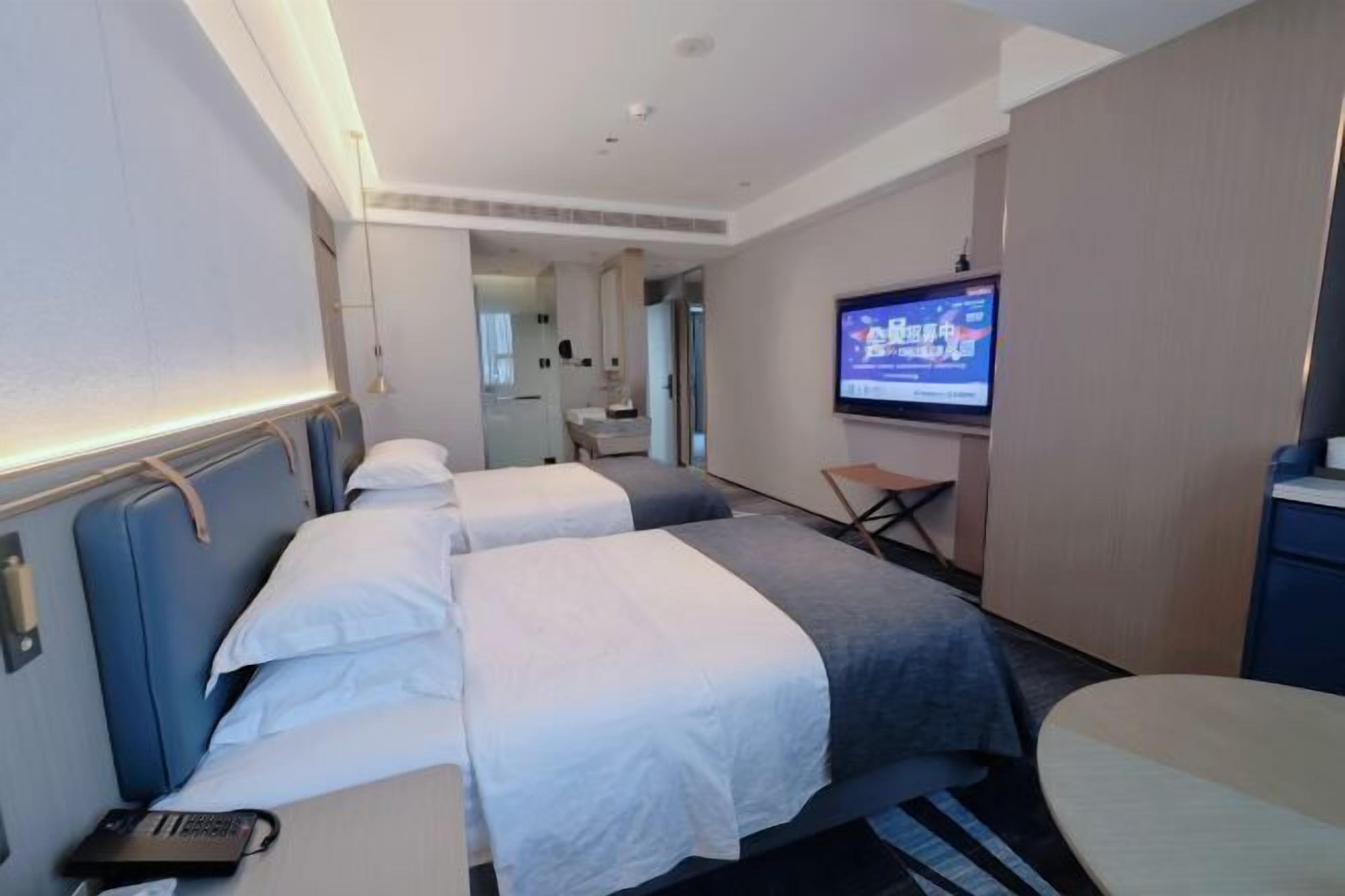 Ett hotellrum med två sängar, ett skrivbord, en stol, en tv och ett badrum som syns genom en öppen dörr.