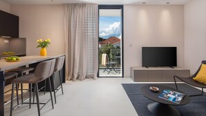 Un salon moderne doté d’un téléviseur à écran plat, d’un coin repas avec une table et des chaises, et d’une grande fenêtre agrémentée de rideaux.
