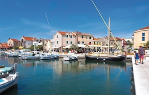 Un port de plaisance où sont amarrés plusieurs bateaux, une jetée où se promènent des gens, et des bâtiments aux toits rouges.