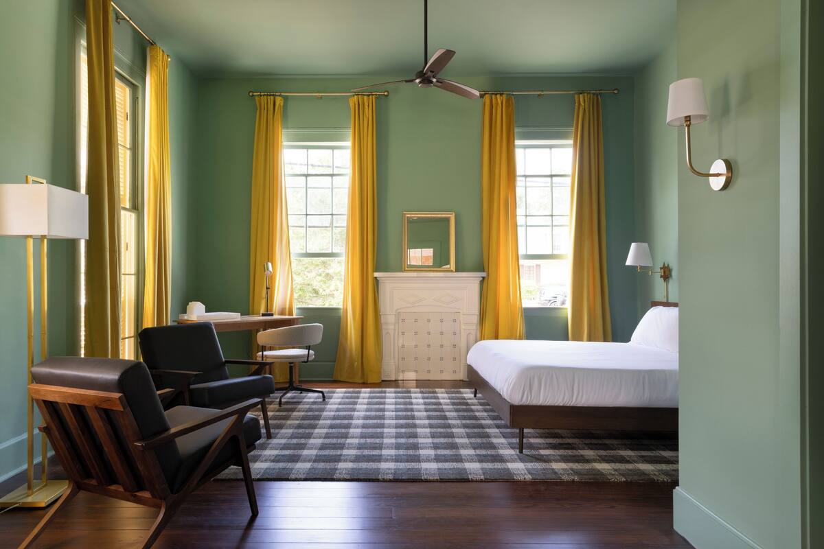 Ein Hotelzimmer mit Bett, Schreibtisch, Stuhl, Deckenventilator und Kamin.