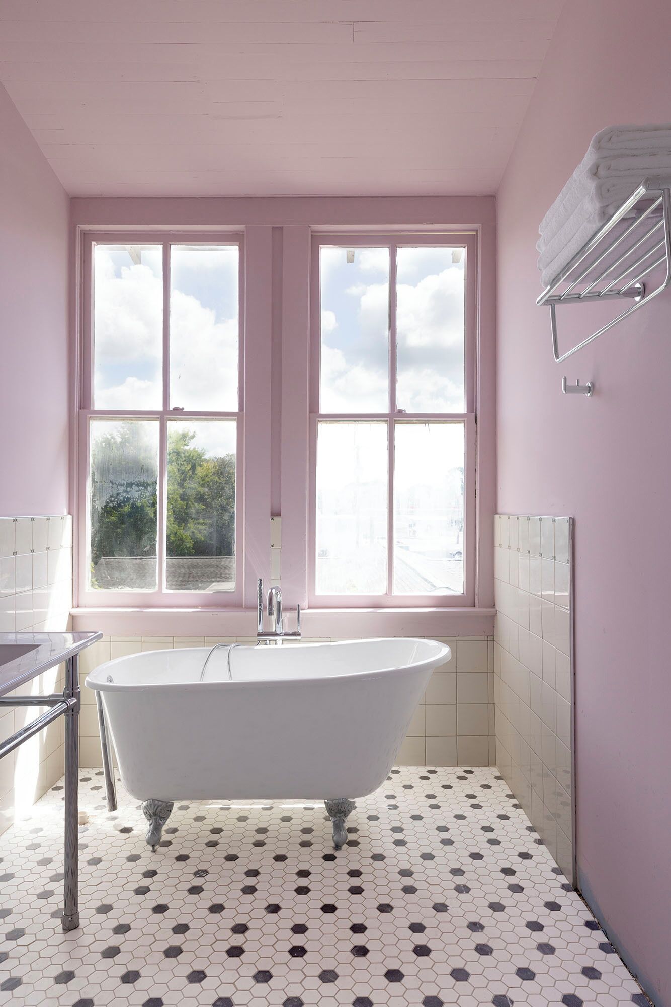 Un baño con una bañera independiente, dos ventanas, un perchero y suelo de baldosas.
