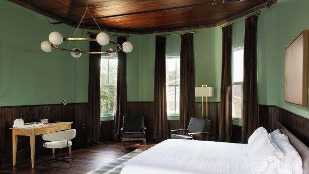 Une chambre d’hôtel avec un grand lit, un bureau avec une chaise, une chaise supplémentaire et une lampe.