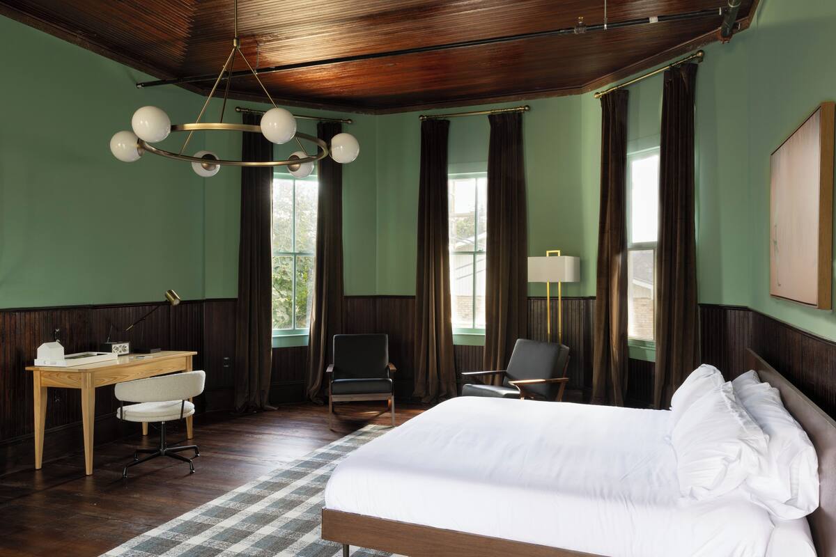 Ein Hotelzimmer mit einem großen Bett, einem Schreibtisch mit Stuhl, einem zusätzlichen Sessel und einer Lampe.
