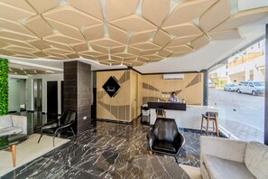 Een moderne lobby met een marmeren vloer, een receptiebalie en een zithoek met een bank en stoelen.