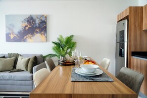 Een eethoek met een houten tafel, stoelen, een schaal, borden en een potplant.