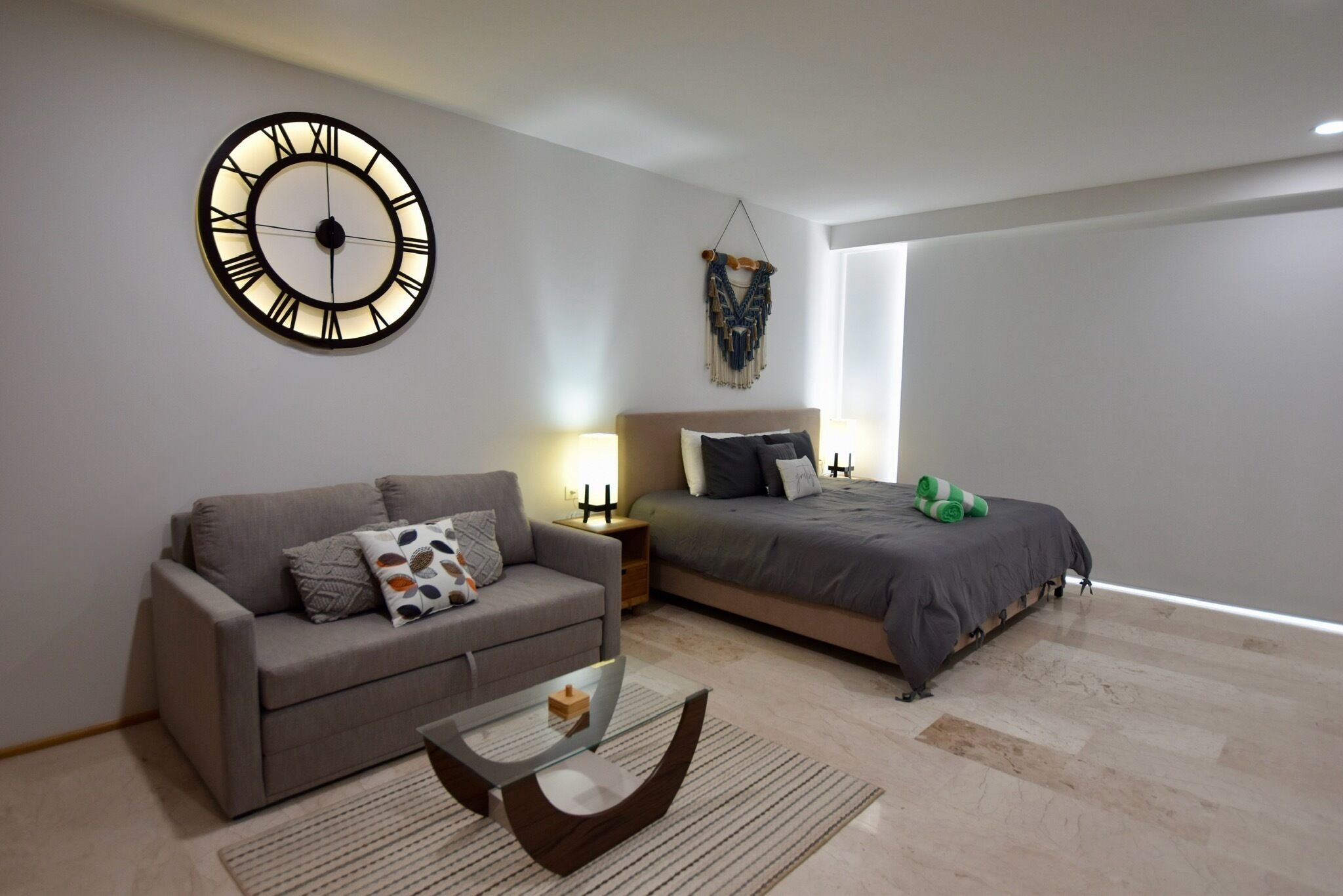 A modern bedroom with a large bed, a sofa, a coffee table, and a wall clock.
