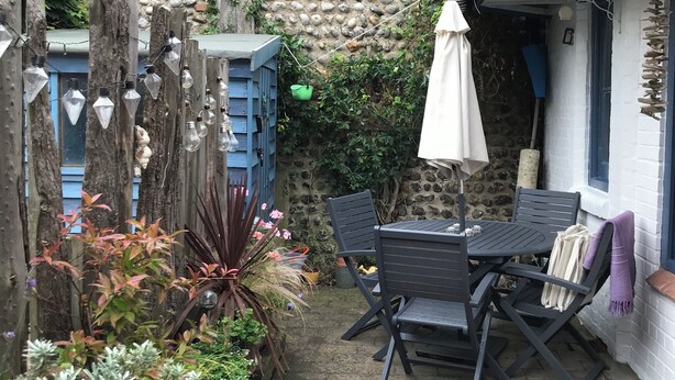 A patio area with a stone wall, a table with chairs, and a hanging umbrella. - Cosy seaside cottage one minute walk from the beach. Dog friendly! (Cromer)
