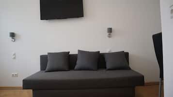 A modern room with a dark sofa, a flat-screen TV mounted on the wall, and two wall-mounted lamps.