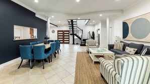 A modern living room with a dining area, a staircase, and a large abstract painting.