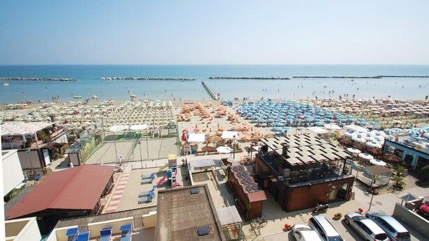 Un hotel frente a la playa con varias habitaciones, piscina y vistas al mar.