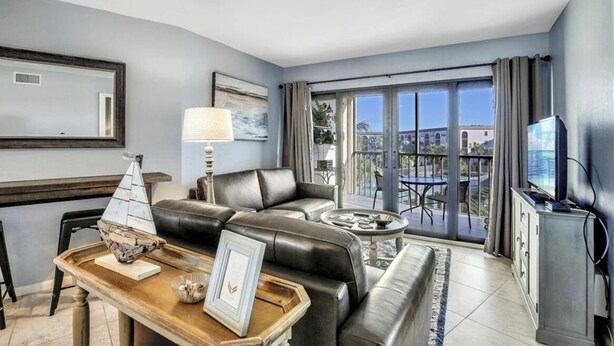 Ein modernes Wohnzimmer mit Ledersofa, Couchtisch und Fernseher. Ein Balkon bietet Blick auf die Stadt.