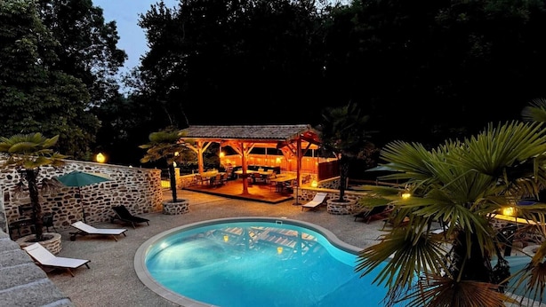 Piscina com espreguiçadeiras, parede de pedra e área coberta com mesas e cadeiras.