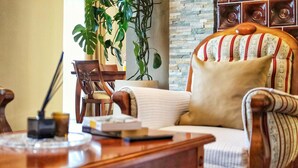 Un escritorio de madera con una lámpara, una silla con tapicería a rayas y una planta grande al fondo.