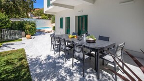 Un patio con mesa y sillas, una piscina y un edificio blanco con contraventanas verdes.