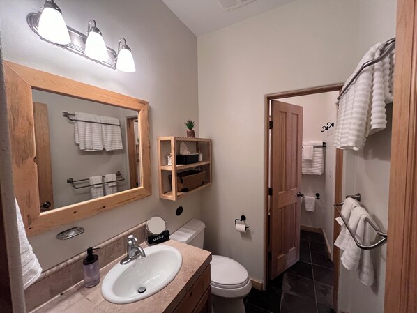 A bathroom with a wooden vanity, a sink, a mirror, a toilet, and a shower area.