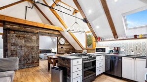 A kitchen with a central island, wooden beams, a clock, and a window.