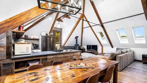 A modern loft-style kitchen with a wooden dining table, built-in appliances, and a lofted seating area with a view.