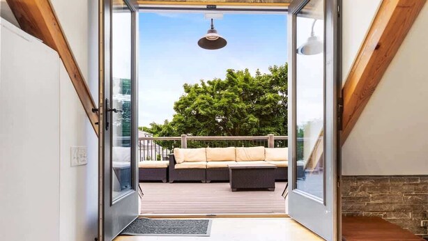 A modern interior with a glass door leading to an outdoor deck with a sofa and a dining table.