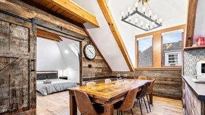 A dining area with a wooden table and chairs, a clock on the wall, and a kitchen area with a coffee machine.