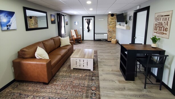 A modern living room with a brown leather sofa, a white coffee table, a wooden dining table with chairs, a brick accent wall, and a mounted TV. - Charming building with 1 bedroom and AC, WiFi in serene Whitehall (Whitehall)