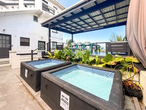 Two hot tubs with a sign indicating temperature range, surrounded by tropical plants and a covered seating area.