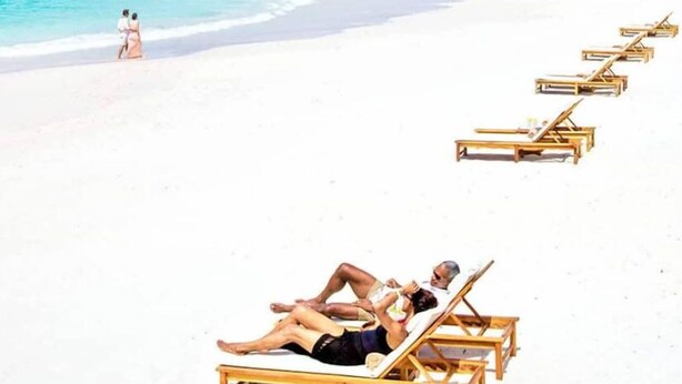 A beach with white sand and clear blue water. There are wooden lounge chairs lined up on the sand. - Studio APT 4B, Oceanview + Pool, Near Beach  @ Paradise Point Barbados (Oistins)