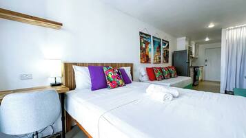 Habitación de hotel con dos camas, un escritorio y una silla. Hay almohadas coloridas y un cartel en la pared.