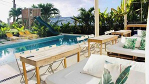 A poolside area with lounge chairs, a table, and a slide. - Studio APT 4B, Oceanview + Pool, Near Beach  @ Paradise Point Barbados (Oistins)