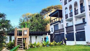 A multi-story building with balconies, a wooden play structure, and lush greenery. - Studio APT 4B, Oceanview + Pool, Near Beach  @ Paradise Point Barbados (Oistins)