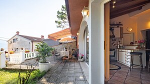 A cozy outdoor patio with a stone floor, a dining table, and chairs. There is a small garden area with potted plants and a view of neighboring buildings. - Stunning home in Rijeka with WiFi (Rijeka)
