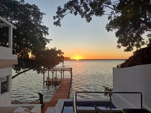 A sunset view from a modern building with a wooden deck extending over water, a pool, and a staircase leading to the deck. - ZENSUS LAGUNA (Bacalar)