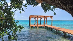 A wooden pier extending into clear turquoise water, supported by wooden posts, with a simple wooden structure at the end. - ZENSUS LAGUNA (Bacalar)