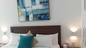 A neatly made bed with white and teal bedding, a teal throw pillow, and a white towel folded at the foot of the bed. There is a nightstand with a lamp and a phone on it. - ZENSUS LAGUNA (Bacalar)